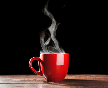 red mug on table with steam rising from mug